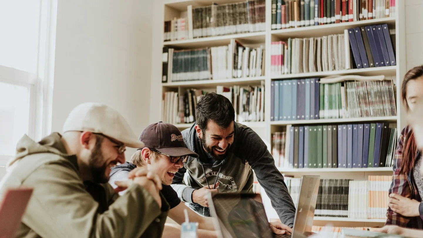 Colleagues gather around a laptop in a room lined with bookshelves.