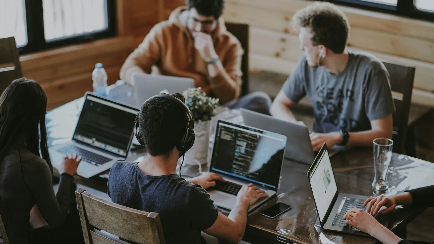 A team works together on laptops around a long wooden table.