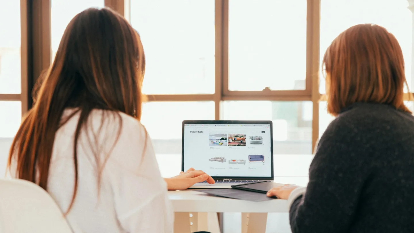 Two women review a website together on a laptop.