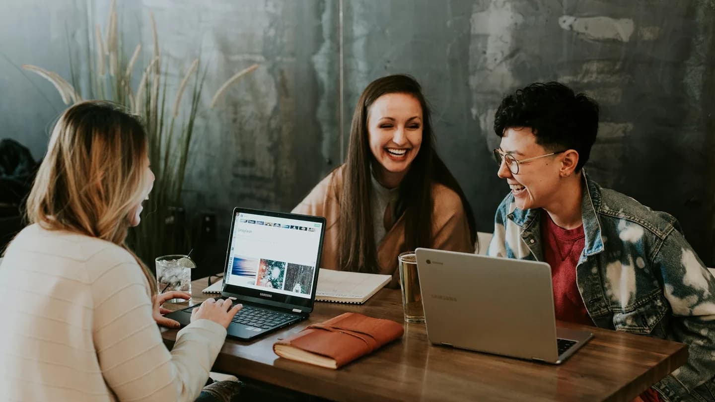 Three people share ideas with laptops and notebooks at a cafe table.